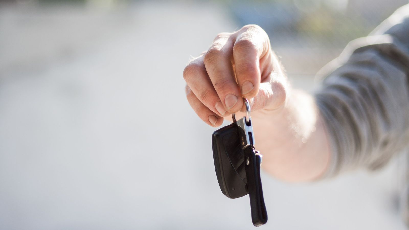 Hand hält einen Autoschlüssel zur Übergabe hin